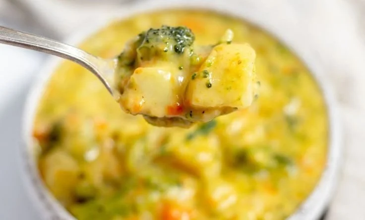 Bowl of creamy Broccoli Potato Cheese Soup garnished with cheese and broccoli florets.