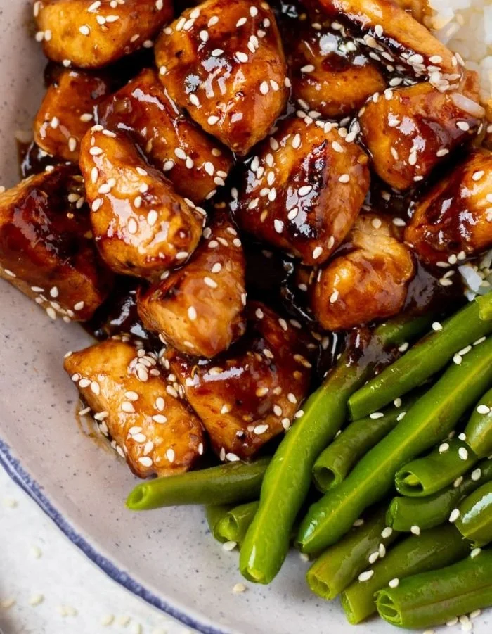 High protein sesame chicken dish garnished with sesame seeds and green onions.