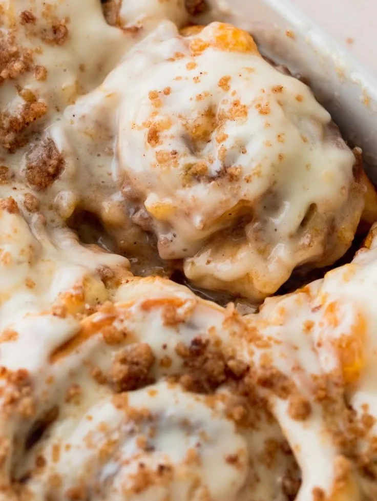 Freshly baked peach cobbler cinnamon rolls topped with icing and peaches
