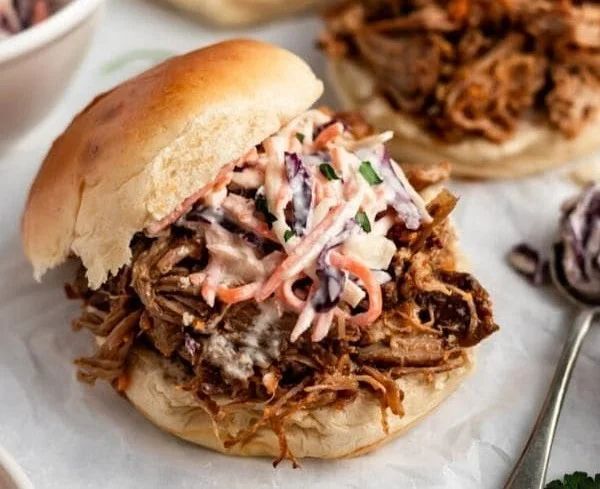 Delicious slow cooker pulled pork served on a platter with barbecue sauce and buns.