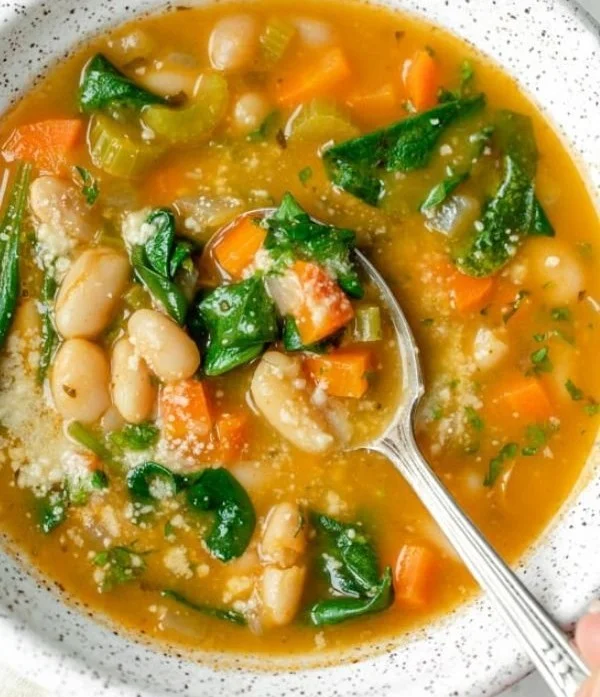 A bowl of vegetarian Mediterranean white bean soup garnished with herbs and vegetables.