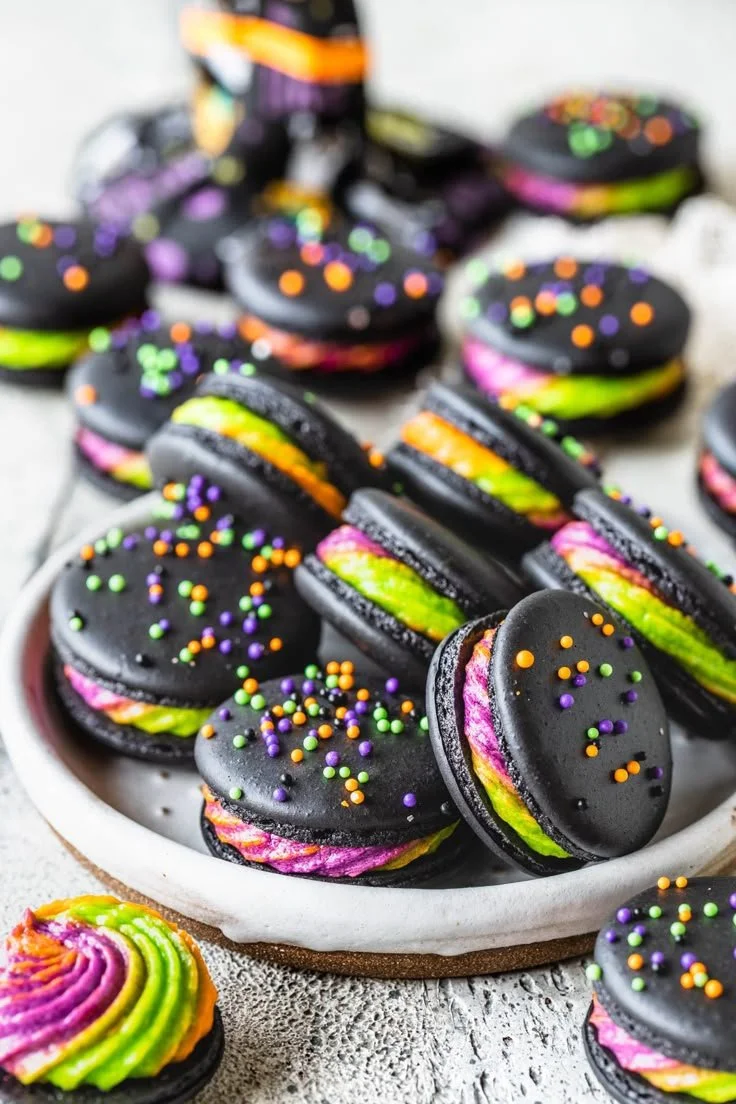 Black macarons filled with tricolor ermine buttercream on a decorative plate.